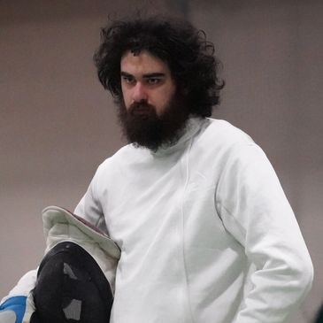 Fencer in white gear holding mask and sword, focused and ready.