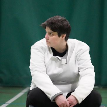 Person in white jacket sitting on a sports court looking down.