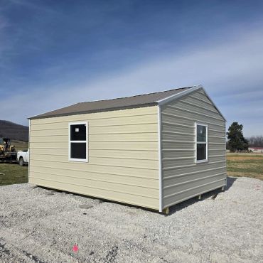 Small beige metal building on gravel with windows under a blue sky.