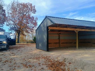 Open metal shed with wooden beams and autumn trees in the background.