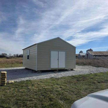 Metal storage shed on a gravel pad under a partly cloudy sky.
