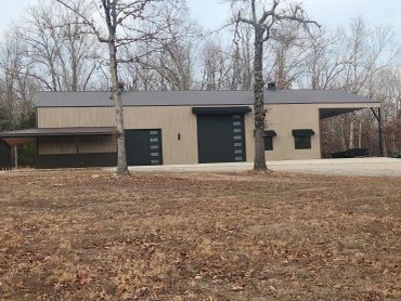 Modern barn-style building with metal exterior and large doors in a wooded area.