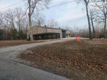 A modern barn-like building on a gravel driveway surrounded by leafless trees.