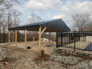 A newly constructed open metal carport with wooden supports in a rural setting.