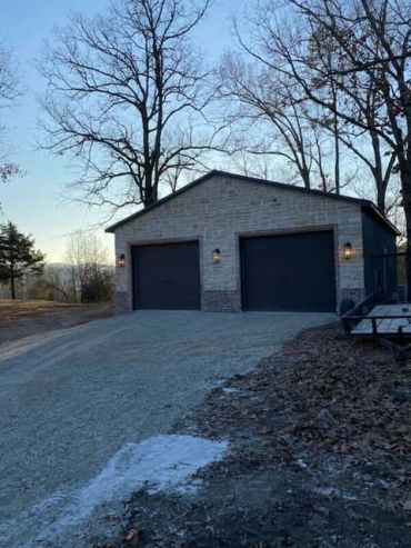 Stone garage with two dark garage doors on a gravel driveway.
