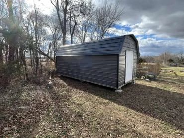 A black metal shed in a backyard with a white door.