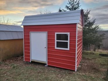 Small red garden shed with white trim and a window at sunset.