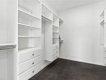 Empty white walk-in closet with shelving and drawers.