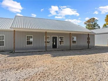 A modern metal building with a covered porch on a gravel lot.