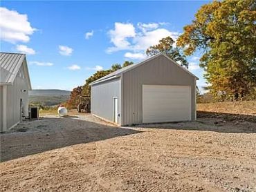 A gray metal garage with a closed white door on a gravel driveway.
