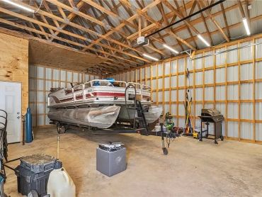 Pontoon boat stored inside a spacious metal garage or workshop.