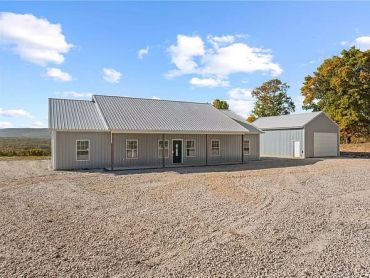 Metal house and detached garage on a gravel lot under a bright sky.