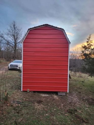 Red barn-style shed on a grassy yard during sunset.