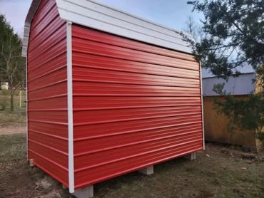 Red and white metal shed on concrete blocks in a yard.