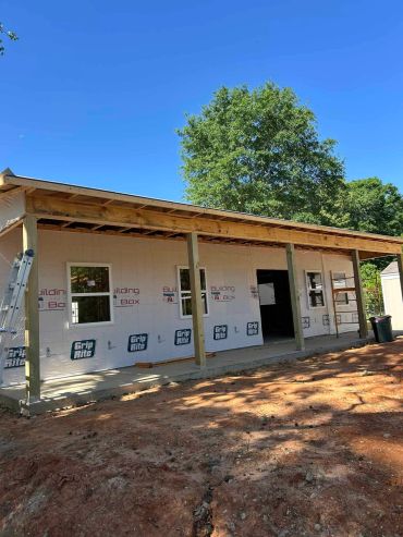 Partially constructed building with wooden roof frame and concrete foundation under clear blue sky.