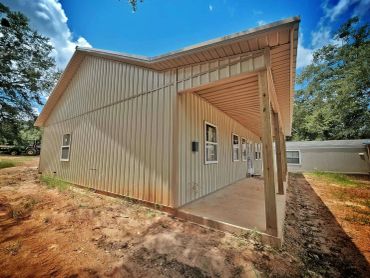 Newly constructed beige metal building with windows and a porch beneath a clear blue sky.