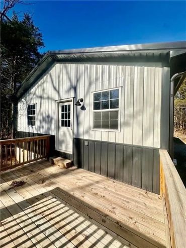 A small house with a wooden deck and two windows on a sunny day.