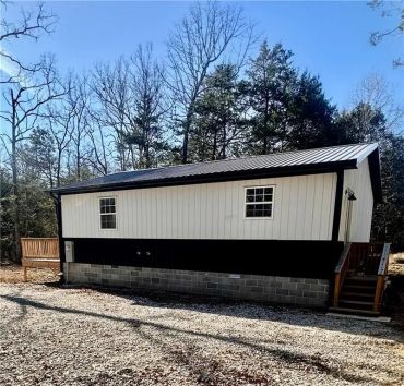 A modern black-and-white cabin with a metal roof in a wooded area.