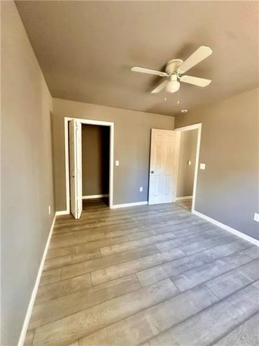 Empty room with wooden flooring, neutral walls, ceiling fan, and two doors.