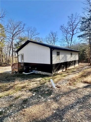 Small white and black house in a wooded area on a sunny day.