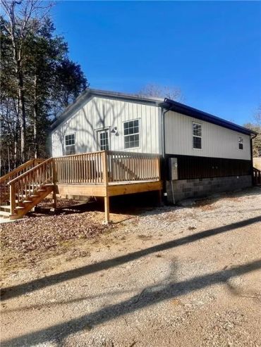A modern single-story house with a wooden deck and stairs under a clear blue sky.
