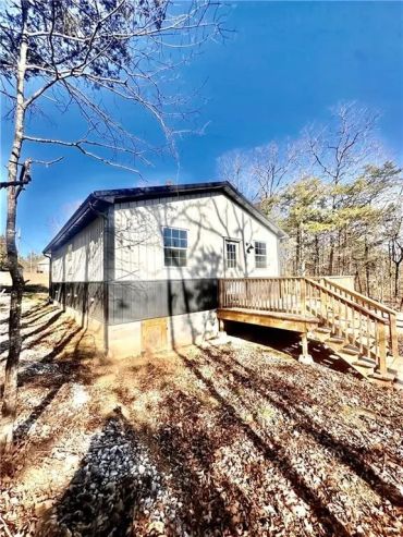 A small cabin with a wooden deck surrounded by trees under a clear blue sky.