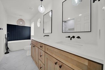 Modern bathroom with wood cabinetry, dual mirrors, and a freestanding tub.