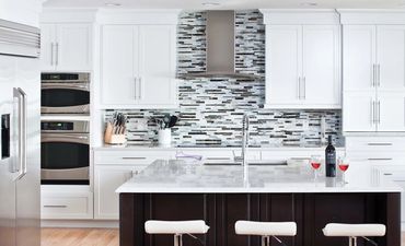 Modern white kitchen with a large island and wine glasses.
