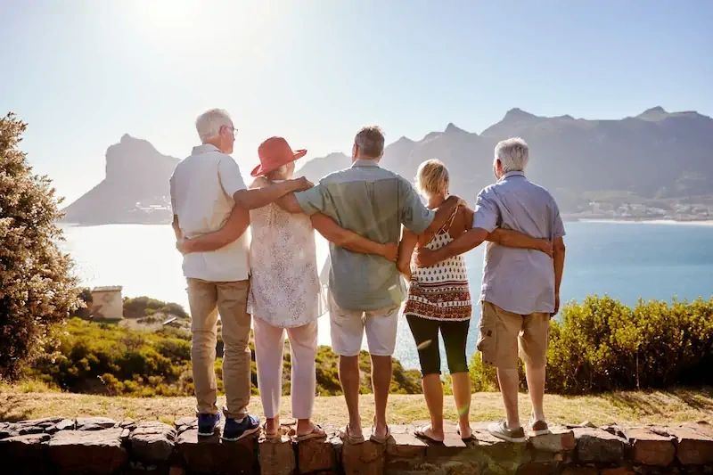 Group of friends embracing on a family reunion by the sea with mountains in the background.