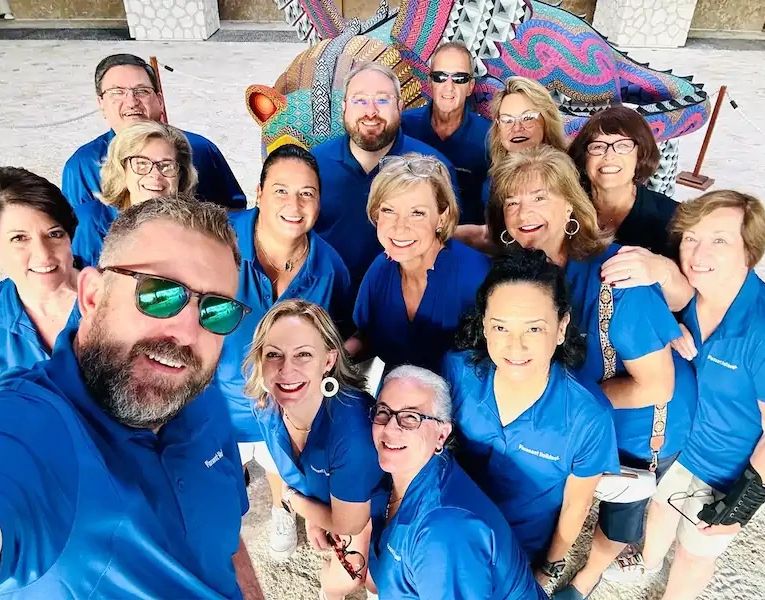 Group selfie of smiling people in matching blue shirts.