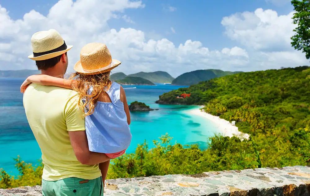 A father and daughter on a family cruise package overlooking a blue lagoon surrounded by mountains.