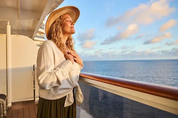 A passenger on a South Pacific voyage enjoying the ocean breeze from a ship deck at sunrise.