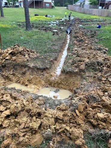 Excavated trench with muddy water and workers in a residential backyard.