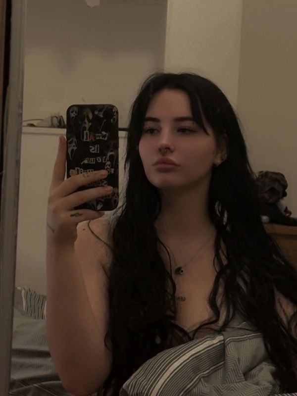 Young woman with long black hair taking a mirror selfie.