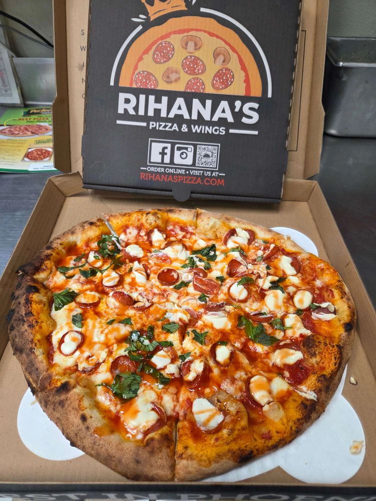 A pepperoni pizza with herbs on top in a Rihana's Pizza box.