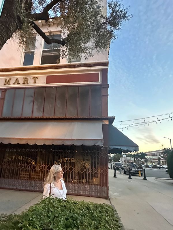 Woman standing in front of an antique store at sunset.