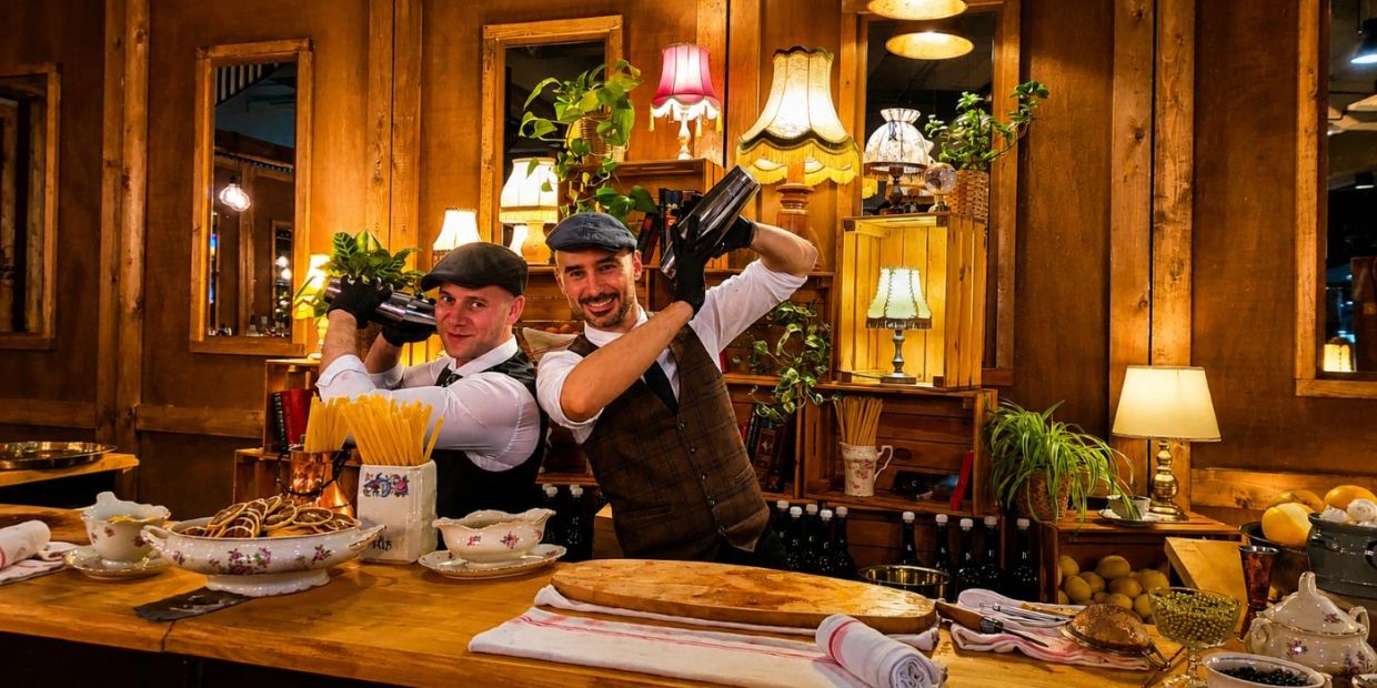 Deux barmans souriants dans un bar en bois rustique.