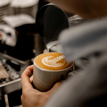 Barista pouring milk to create latte art in a coffee cup.