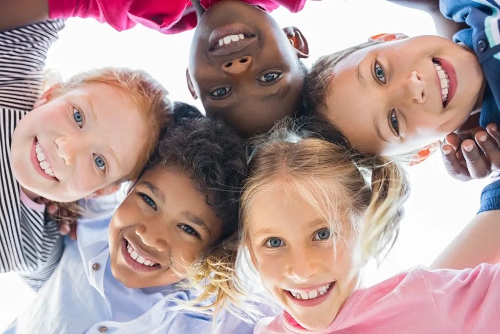 Children smiling looking down at camera in a pinwheel circle formation