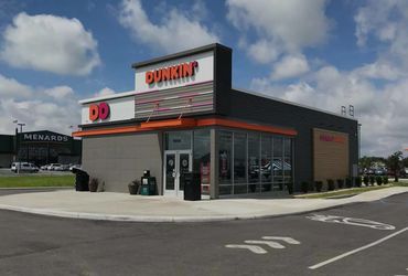 Modern Dunkin' store with clear blue sky and Menards in background.