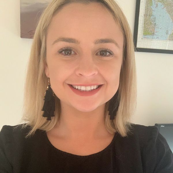 A smiling woman with blonde hair wearing a black top and black tassel earrings.