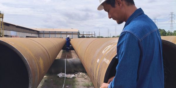 Worker inspecting large metal pipes at construction site.