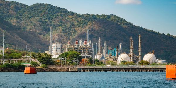 Industrial refinery by the coastline with green hills in the background.