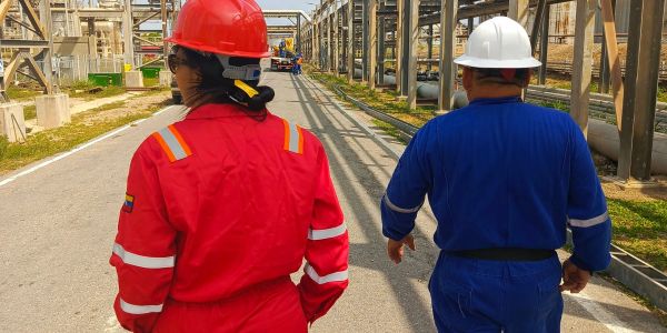 Two workers in safety gear walk through an industrial site.