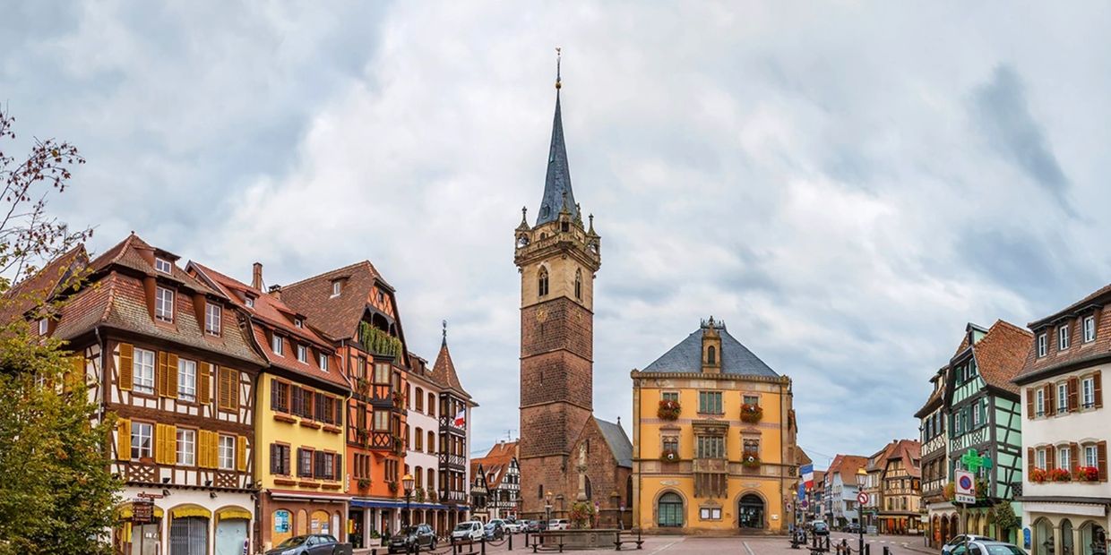 Charming European town square with historic buildings and a tall clock tower under a cloudy sky.
