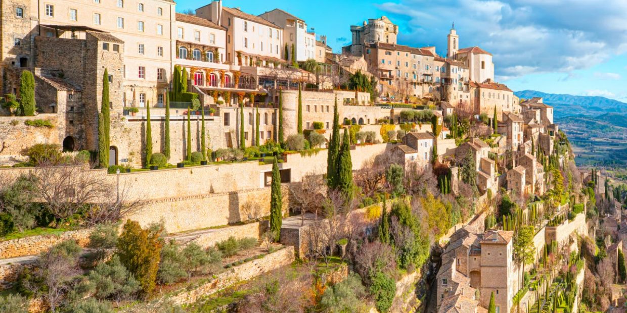 A stunning hillside village with stone buildings and lush greenery under a bright blue sky.