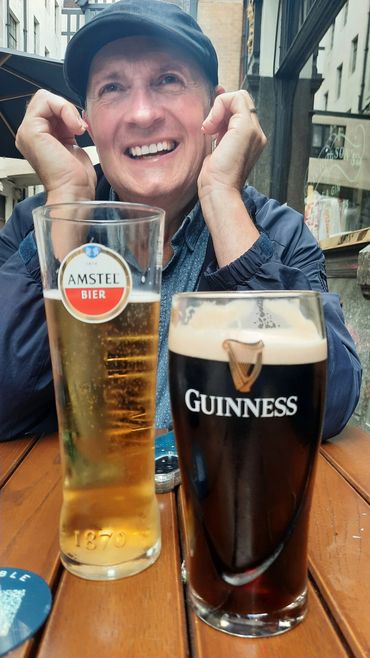 Smiling man enjoying beers at an outdoor table.