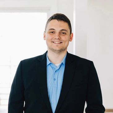 Smiling man in business attire posing indoors with natural light.