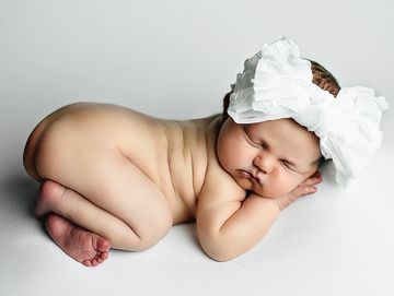 A newborn baby lying on their side on a white 