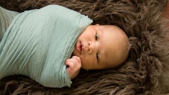Newborn swaddled laying on a piece of fur